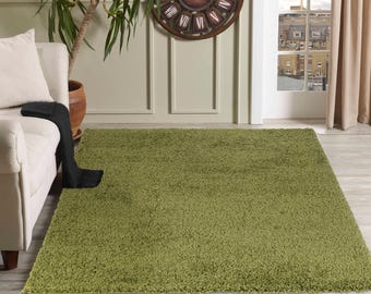 May include: A soft, green shag rug in a living room setting. The rug is placed in front of a white couch and a wall with a clock.