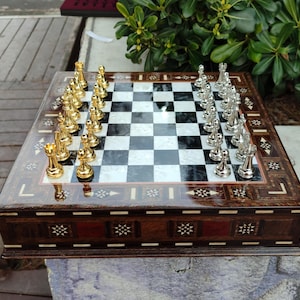 K&ouml;nnte beinhalten: Ein Schachbrett aus Holz mit eingelegten Details und einer schwarz-wei&szlig;en Schachbrettfl&auml;che. Die Schachfiguren sind golden und silbern.