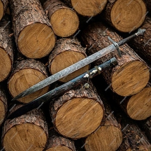 May include: A detailed image of a medieval sword with a patterned blade and a decorative hilt, resting on a pile of wooden logs. The sword is accompanied by a black scabbard with bone-colored accents.
