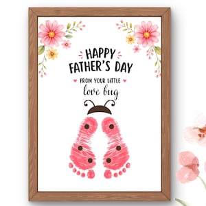 Könnte beinhalten: Ein gerahmter Druck mit dem Text Happy Father's Day From Your Little Love Bug. Das Design zeigt aquarellierte rosa Blumen in den oberen Ecken und zwei rosa Babyfußabdrücke, die mit schwarzen Punkten wie ein Marienkäfer gestaltet sind.