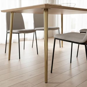 May include: A light wood dining table with gold-colored legs and four gray upholstered chairs with black metal legs. The table is rectangular and appears to be made of solid wood. The chairs have a simple, modern design.