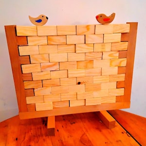May include: A wooden block stacking game with two wooden birds on top. The birds are painted in bright colors, one blue and one red. The game is set up on a wooden base with three legs.