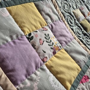 May include: A patchwork quilt with squares of different colors and patterns, including yellow, purple, and gray. The quilt is made of fabric with a floral print and a butterfly design.