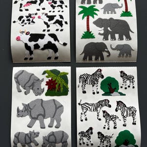 Pode incluir: Quatro folhas de autocolantes de animais. As folhas apresentam vacas, elefantes com palmeiras, rinocerontes e zebras. Os autocolantes são de vários tamanhos e cores, com padrões a preto e branco.