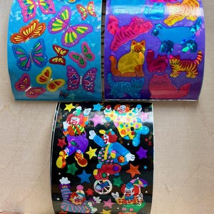 May include: Three rolls of colorful stickers featuring various designs. One roll has butterflies in shades of pink, yellow, and green on a blue background. Another roll displays cats in orange, pink, and blue on a purple background. The third roll showcases clowns on a black background.