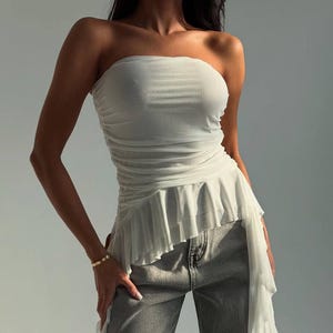 May include: A white mesh tube top with a ruffled hem and a long, flowing train. The top is worn with gray jeans.