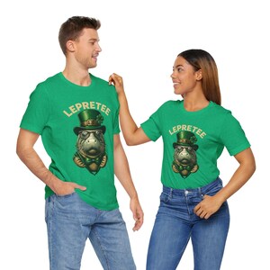 May include: Two people wearing green t-shirts with a cartoon leprechaun manatee wearing a hat and holding a pot of gold. The text on the shirts says "Lepretee".