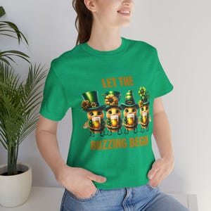 May include: Green t-shirt with a graphic of four cartoon bees wearing green hats and holding glasses of beer. The text "Let the Buzzing Begin" is printed below the bees.