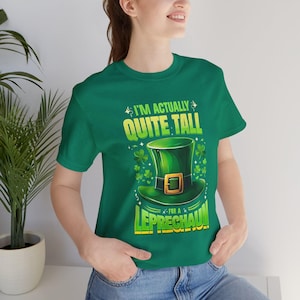 May include: Green t-shirt with the text "I'M ACTUALLY QUITE TALL FOR A LEPRECHAUN!" and a graphic of a green leprechaun hat with a gold buckle and shamrocks. The shirt is a solid green color.