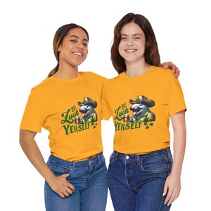 May include: Two people wearing yellow t-shirts with a green cartoon manatee wearing a hat and holding a beer. The text on the shirts says "Go Luck Yerself".