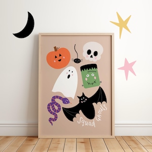 May include: A framed print with Halloween illustrations. It features a smiling orange pumpkin, a white ghost, a purple snake, a black spider, a skull, a green Frankenstein's monster, and a black bat. The words "Squad Ghouls" are written on the bottom.