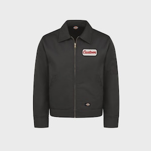 Puede incluir: Chaqueta de trabajo negra con cierre de cremallera y cuello. La chaqueta tiene un parche con la palabra "Custom" en escritura roja. También tiene dos bolsillos delanteros y un pequeño parche con el logotipo cerca del dobladillo.