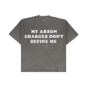 May include: A gray t-shirt with the text "MY ARSON CHARGES DON'T DEFINE ME" in white block letters. The shirt has short sleeves and a crew neck. The fabric appears to be pre-shrunk.