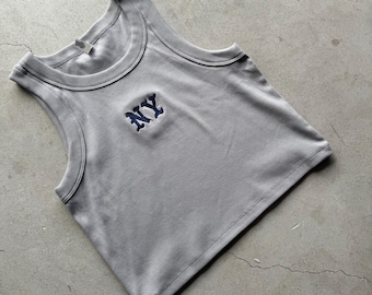 May include: A light gray cropped tank top with a blue embroidered "NY" on the front.