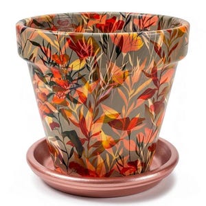 May include: A tapered ceramic plant pot featuring a botanical print of orange, red, and yellow leaves and flowers against a muted gray background, paired with a matching metallic copper-toned circular saucer base for drainage and stability.