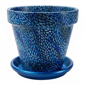 May include: A tapered plant pot with a repeating blue and teal leaf-like pattern across the exterior surface. The pot features a wide, thick rim and sits on a matching solid metallic blue circular saucer, creating a cohesive set for indoor plants.