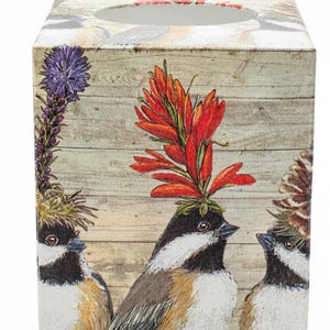 May include: A square tissue box cover featuring a light wood grain background with three birds. Each bird has a different botanical element on its head, including a tall purple flower, a bright red flower, and a brown pinecone-like cluster.