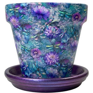 May include: A tapered plant pot with a matching saucer, featuring a vibrant pattern of purple flowers and teal dragonflies against a blue and green background. The saucer has a solid metallic purple finish, while the pot is decorated throughout.