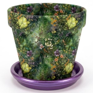 May include: A tapered plant pot featuring a dense, colorful botanical print of green foliage, yellow blossoms, purple flowers, and small orange buds. The pot sits on a solid, metallic purple circular saucer against a plain white background.