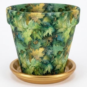 May include: A tapered plant pot featuring a dense, overlapping pattern of green and yellow autumn leaves. The pot sits on a solid, metallic gold-colored circular saucer. The design covers the entire exterior surface of the pot, creating a lush, foliage-inspired appearance with varied shades of forest green, lime, and golden yellow tones.