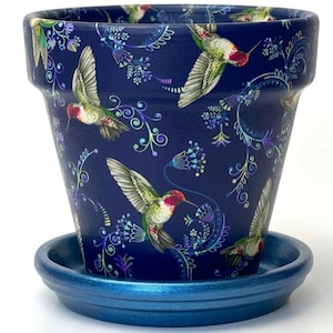 May include: A deep navy blue flower pot with a matching saucer, featuring a repeating pattern of colorful hummingbirds in flight surrounded by intricate, swirling floral vines in shades of purple, green, and light blue across the exterior surface.
