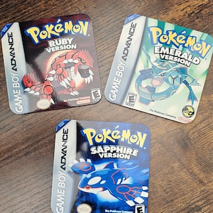 May include: Three Pokémon Game Boy Advance coasters. The coasters feature the game titles: Ruby Version, Emerald Version, and Sapphire Version. Each coaster has a different Pokémon character and the Game Boy Advance logo.