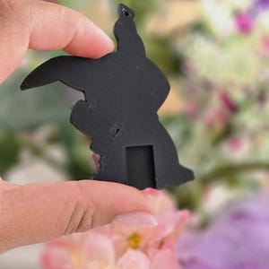 Peut inclure: Un pendentif plat en forme de silhouette noire mate repr&eacute;sentant un personnage de dessin anim&eacute; avec de longues oreilles, une t&ecirc;te arrondie et une petite d&eacute;coupe rectangulaire &agrave; la base. Il poss&egrave;de un petit trou circulaire en haut.