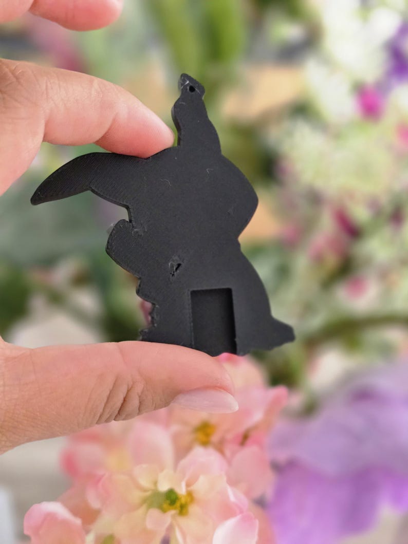 Peut inclure: Un pendentif plat en forme de silhouette noire mate repr&eacute;sentant un personnage de dessin anim&eacute; avec de longues oreilles, une t&ecirc;te arrondie et une petite d&eacute;coupe rectangulaire &agrave; la base. Il poss&egrave;de un petit trou circulaire en haut.
