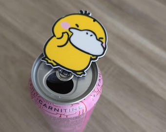 Peut inclure: Un personnage de canard jaune de dessin animé avec un bec blanc et des joues roses fixé à la languette argentée d'une canette de boisson rose en aluminium. La canette présente du texte visible, dont le mot CARNITINE imprimé en foncé.