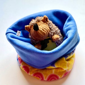May include: A blue fleece fabric dog bed with a colorful floral pattern on the bottom. A brown and gray hedgehog plush toy is inside the bed.