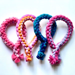 May include: Three colorful braided rope dog toys in pink, orange, and blue. Each toy is shaped like a loop with a knotted end.