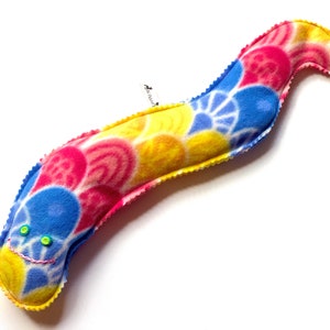 May include: A long, colorful, tie-dye patterned plush worm with a stitched-on face and green eyes.