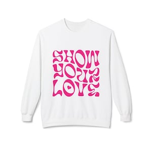 Könnte beinhalten: Weißer Langarm-Pullover mit einer pinkfarbenen Grafik, auf der "SHOW YOUR LOVE" in einer retro-psychedelischen Schrift steht.