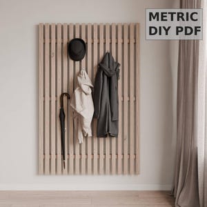 May include: A wooden slat wall mounted coat rack with a black hat, a beige coat, a black coat, and a black umbrella hanging on hooks. The text "METRIC DIY PDF" is in the upper right corner of the image.