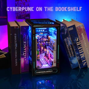 May include: A miniature cyberpunk diorama with a detailed street scene, illuminated by blue and purple lights, is displayed between several books. The books have titles like "A-Declining Steel Town" and "Alliance". The diorama has the text "Cyberworldworld".