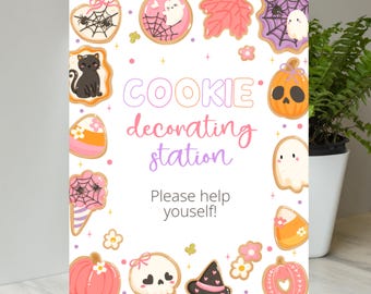 May include: A rectangular sign with a white background, featuring a "Cookie Decorating Station" theme. The sign is decorated with cartoon cookies shaped like pumpkins, ghosts, and spiders. The text "Please help yourself!" is also included.