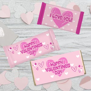 May include: Pink Valentine's Day candy bars with heart and text designs. One bar says "I Love You!" and the others say "Happy Valentine's Day". White hearts and decorative elements are scattered around the bars.