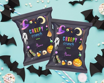 May include: Two black snack bags with "Creepy Crunch" text and Halloween illustrations of a witch's hat, ghost, pumpkin, and broom. Paper bats, marshmallows, and straws surround the bags on a light blue background.