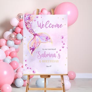 Può includere: Benvenuti alla festa di compleanno di Sabrina, la nostra sirenetta di 6 anni, un cartello con un'illustrazione di coda di sirena viola e rosa, stelle dorate scintillanti e bolle bianche perlate su uno sfondo rosa acquerellato.