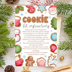 Puede incluir: Una tarjeta de instrucciones para un kit de galletas navideñas con ilustraciones de galletas decoradas, incluyendo un muñeco de nieve, Papá Noel y un hombre de jengibre. La tarjeta presenta el texto "COOKIE kit instructions" y copos de nieve.