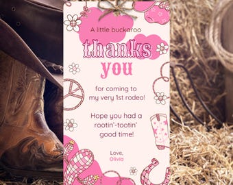 Könnte beinhalten: Eine rosa und weiße Dankeskarte zum Thema Rodeo mit dem Text "Danke" und "für deinen Besuch bei meinem 1. Rodeo!" Die Karte zeigt Illustrationen eines Cowboy-Stiefels, eines Hufeisens und eines Seils. Ein Cowboyhut und ein Stiefel sind im Hintergrund.