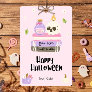 May include: A pink Halloween-themed gift tag with a skull candle, potion bottle, and stacked books that read "you are Spooktacular!". The tag also says "Happy Halloween" and "Love, Sadie". The tag is decorated with small flowers and pumpkins.