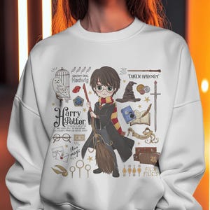 May include: White sweatshirt featuring a cartoon illustration of Harry Potter holding a broom, surrounded by related imagery like an owl, glasses, and the words "Harry Potter" and "I love magic".