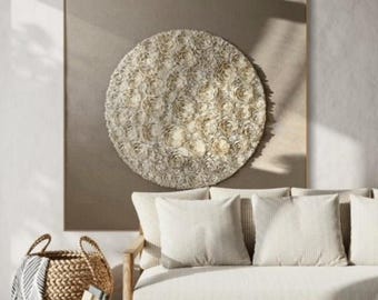 May include: A white sofa with three pillows sits in front of a large framed circular wall art piece with a beige background. The wall art is made of white and beige paper flowers.