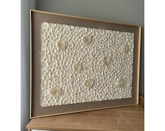 May include: A framed wall art piece featuring a beige background with a textured pattern of white 3D flowers. The flowers are made of a material that resembles seashells.