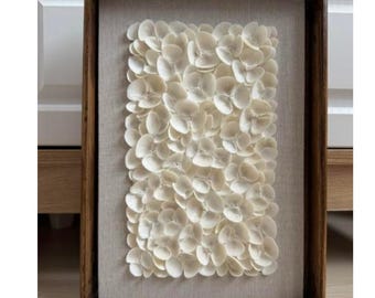 Könnte beinhalten: Ein gerahmtes Wandbild mit einem strukturierten Design aus weißen Blütenblättern. Die Blütenblätter sind in einem dichten, überlappenden Muster angeordnet, das einen 3D-Effekt erzeugt. Der Rahmen ist aus Holz und hat eine natürliche Oberfläche.