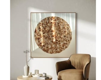 Può includere: Una stampa d'arte astratta incorniciata che presenta un grande design circolare color oro con un effetto testurizzato 3D. La stampa è appesa a una parete bianca sopra una poltrona marrone e un tavolino da caffè in legno.