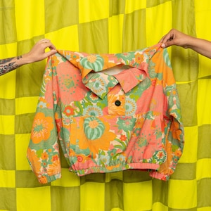 May include: A pink, orange and green floral print jacket with a button closure and a pocket on the front.