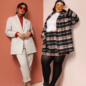 Op de afbeelding: Twee mensen dragen blazers en zonnebrillen. Een persoon draagt een wit topje, een geruite rok, zwarte panty's en zwarte laarzen. De andere persoon draagt een rode top en een beige blazer en broek.