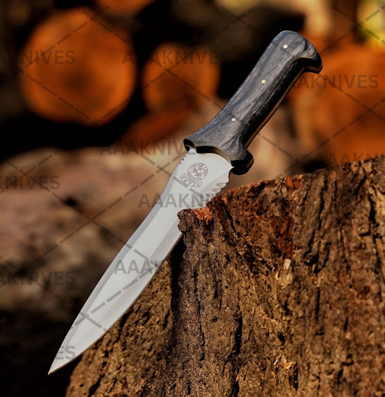 May include: A knife with a polished steel blade and a dark wooden handle. The handle has a curved design and is secured with small silver rivets. The blade has a decorative emblem near the handle. The knife is resting on a tree stump.